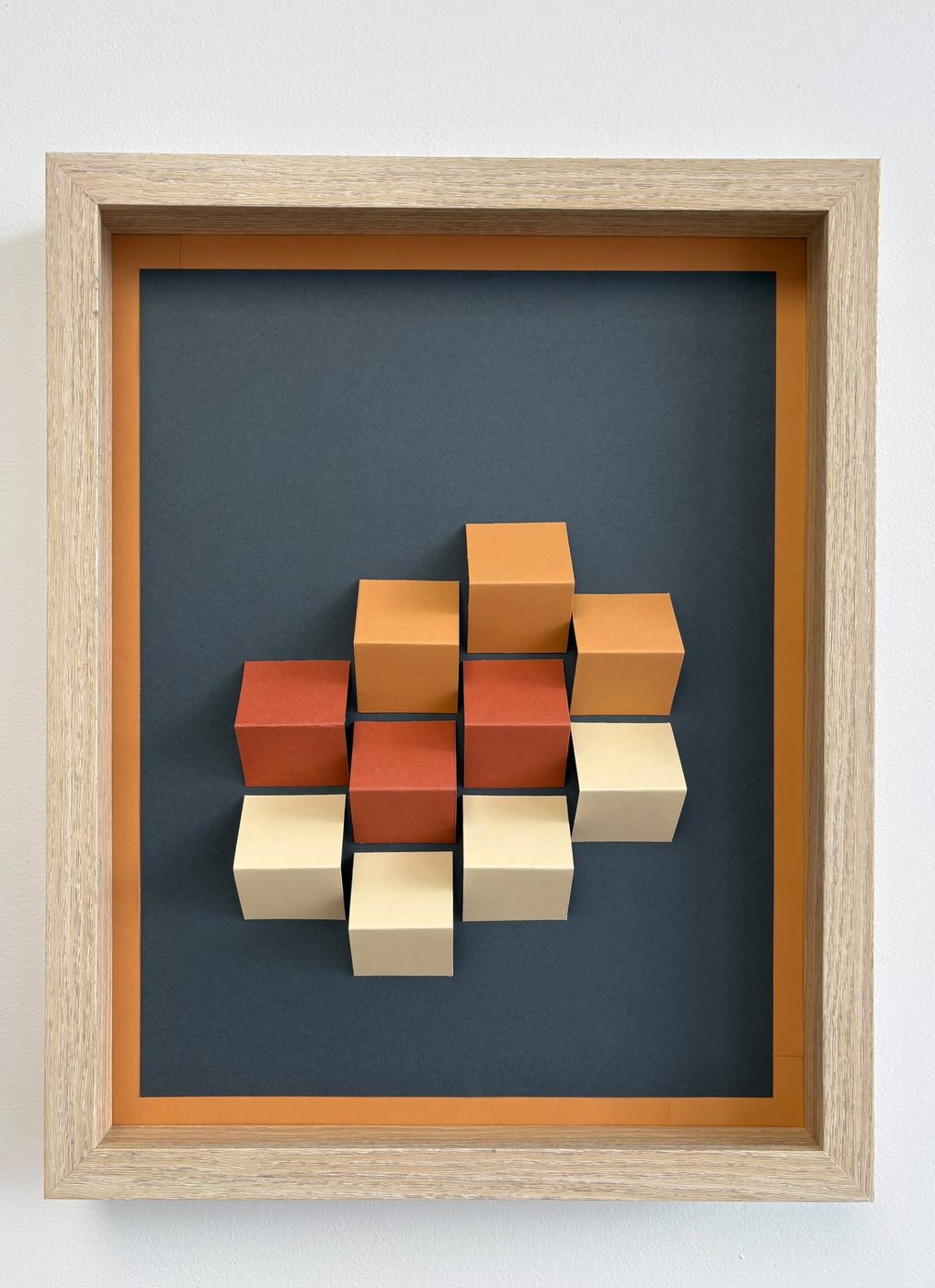 Close-up of a framed 3D cube wall piece in rust, orange and cream