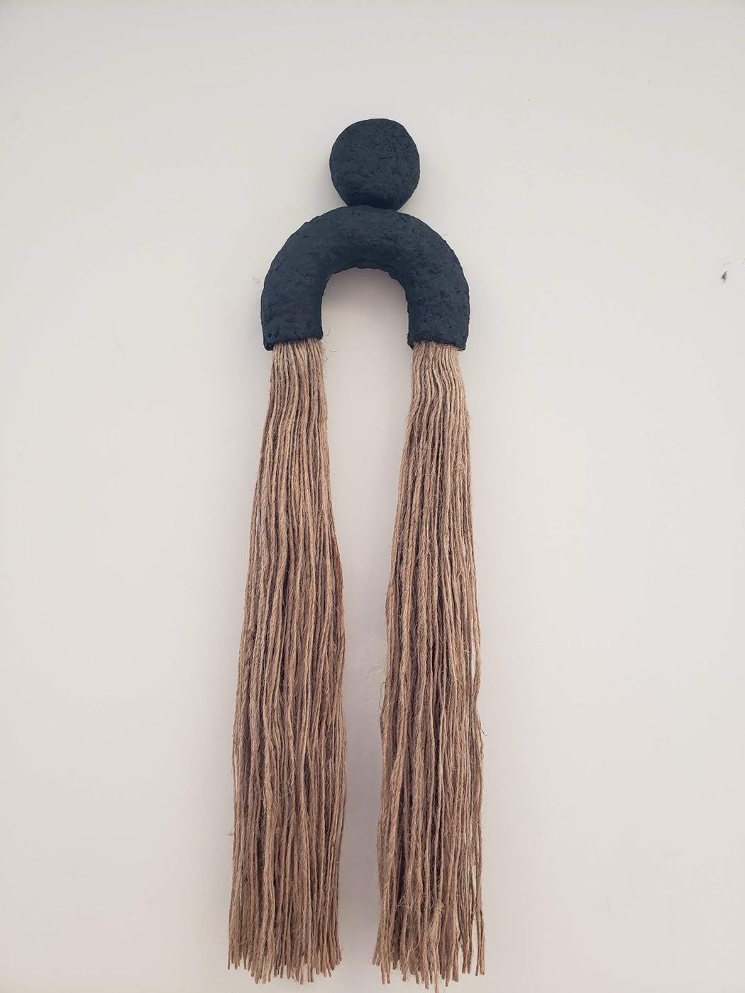 Wall hanging with a black arch shape and beige tassels