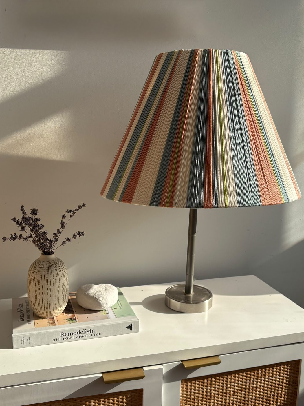 Striped lamp shade styled on a white dresser with rattan baskets